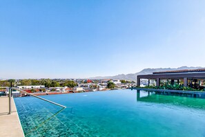Ein klarer, blauer Infinity-Pool mit Blick auf eine Stadt und Berge im Hintergrund.