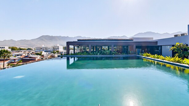 A rooftop infinity pool with a view of mountains and a modern building in the background. - Modern Condo With Rooftop Pool, Balcony, gas Grill & gym Access (Puerto Vallarta)
