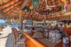 A beachside bar with a thatched roof, wooden chairs, and a pool in the background. - Peaceful Oceanview- Costa Sur Estudio 1 (Puerto Vallarta)