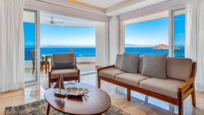 A modern living room with a sofa, armchairs, and a coffee table. Large windows offer a view of the ocean and a distant island. - Stunning 7th-floor Condo With Outdoor Pool, hot tub & bay Views (Puerto Vallarta)