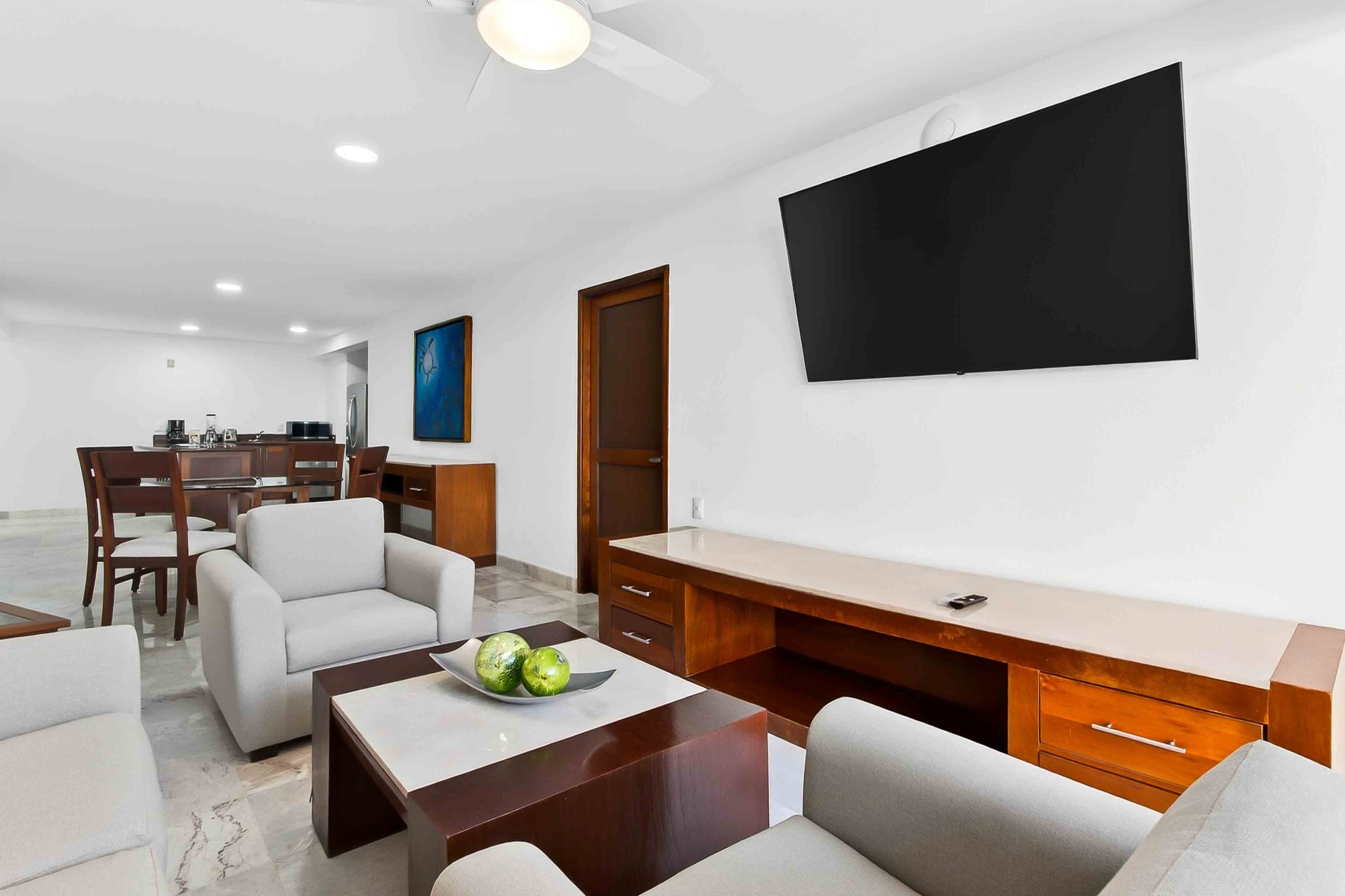 Una sala de estar moderna con televisor de pantalla plana, un escritorio de madera y una zona de comedor con sillas y una mesa.