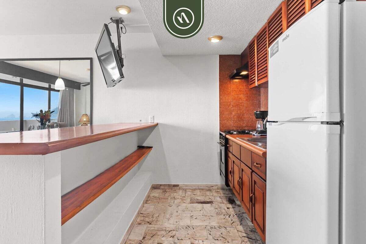 Uma cozinha compacta com geladeira embutida, armários de madeira e uma janela grande com vista para o exterior.
