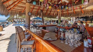 A bar area with wooden furniture, a pool, and a thatched roof. - Costa Sur Suite 2 - Oceanview 1 BR Condo - Pool - Cleaning Included (Puerto Vallarta)