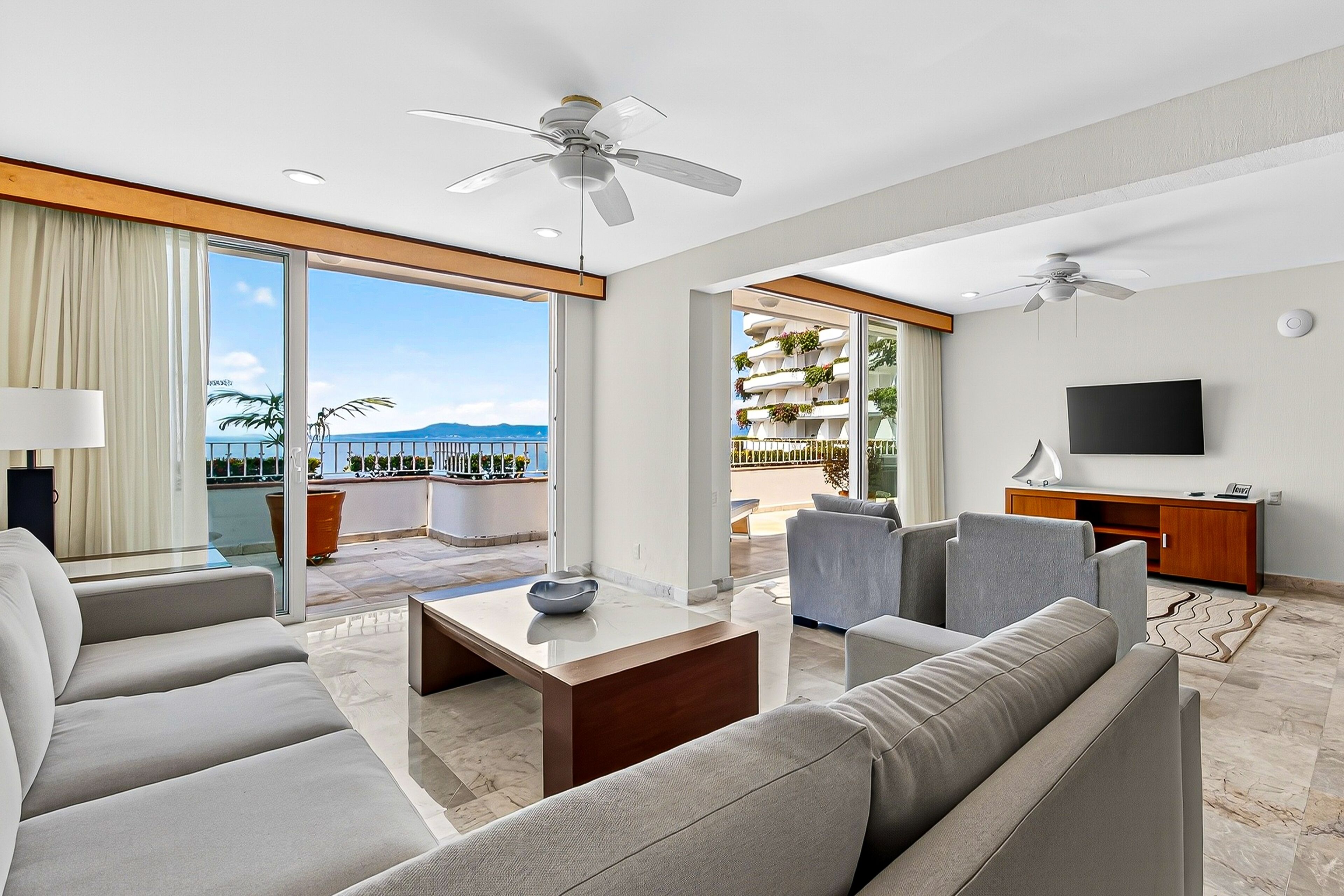 A modern hotel room with a balcony, a flat-screen TV, and a seating area with a coffee table.