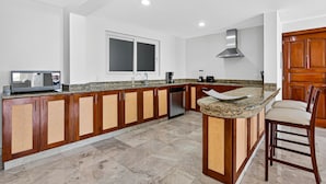 A modern kitchen with wooden cabinets, granite countertops, a built-in dishwasher, and a large window. - Stylish Oceanview Suite With Infinity Pool, Full Kitchen & Bay-view Terrace (Puerto Vallarta)