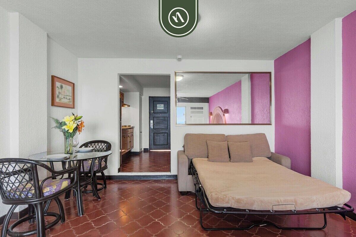 A compact room with a bed, a dining table with chairs, a small kitchen area, and a bathroom visible through an open door.
