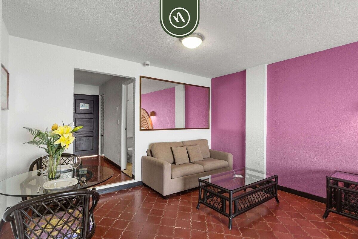 A room with a glass dining table, a sofa, and a mirror on the wall.