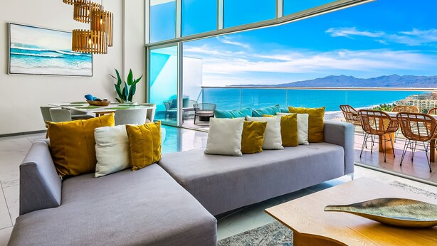 A modern living room with a gray sofa, yellow and white cushions, a wooden coffee table, and a view of the ocean through large windows. - Oceanfront Luxury With Amazing View, 4 Pools, Private Beach, On-site Spa, Dining (Nuevo Nayarit)