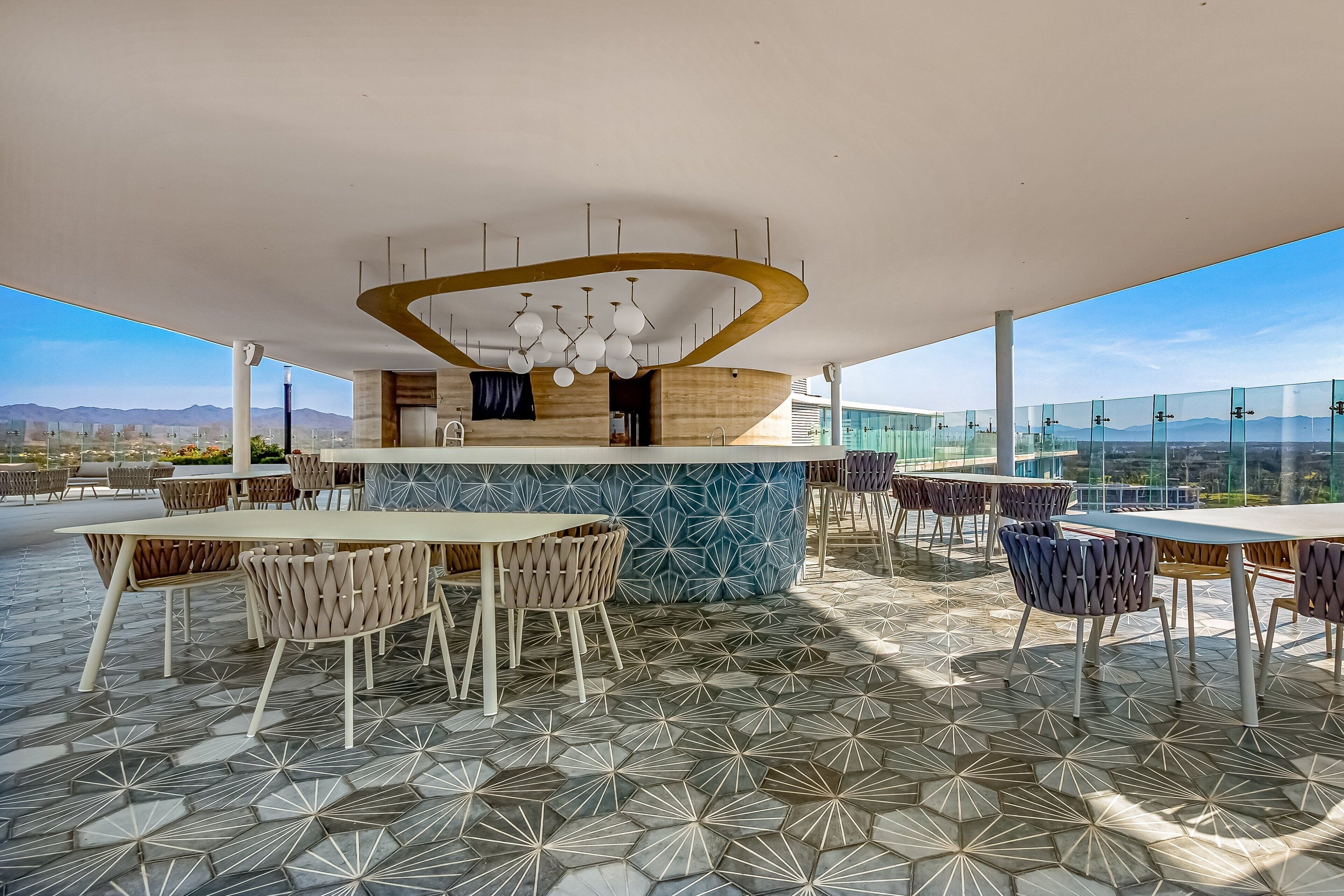 An outdoor dining area with a modern bar, patterned flooring, and a view of the city and mountains.