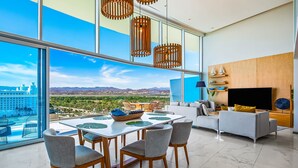 A modern living room with a large TV, a sofa, and a dining area with a table and chairs. - Oceanfront Luxury With Amazing View, 4 Pools, Private Beach, On-site Spa, Dining (Nuevo Nayarit)