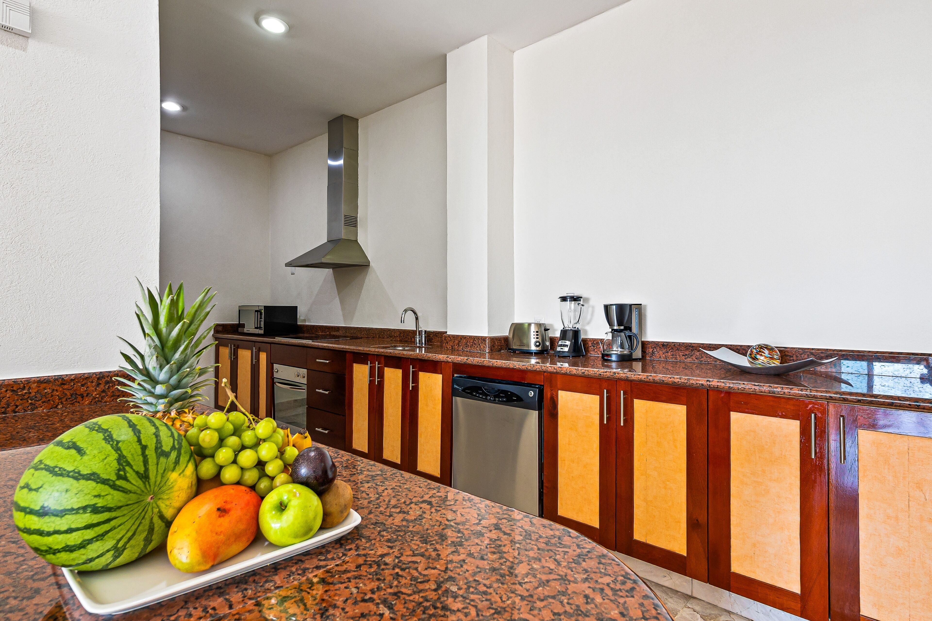 Une cuisine dotée de plans de travail en granit, de meubles en bois, d’un lave-vaisselle en acier inoxydable et d’un présentoir à fruits.