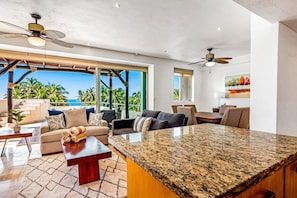 Amplia sala de estar con una gran isla de cocina, ventiladores de techo y vista al océano.