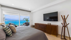 A bedroom with a bed, a TV, a wooden dresser, and a balcony with a view of the sea. - Bright Oceanfront Condo With Balcony, Rooftop Pool & Near Malecon Boardwalk (Puerto Vallarta)