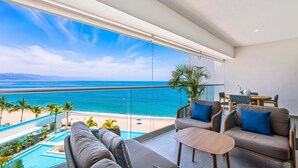 A balcony with a view of the ocean, a pool, and a seating area with a table and chairs. - Bright Oceanfront Condo With Balcony, Rooftop Pool & Near Malecon Boardwalk (Puerto Vallarta)