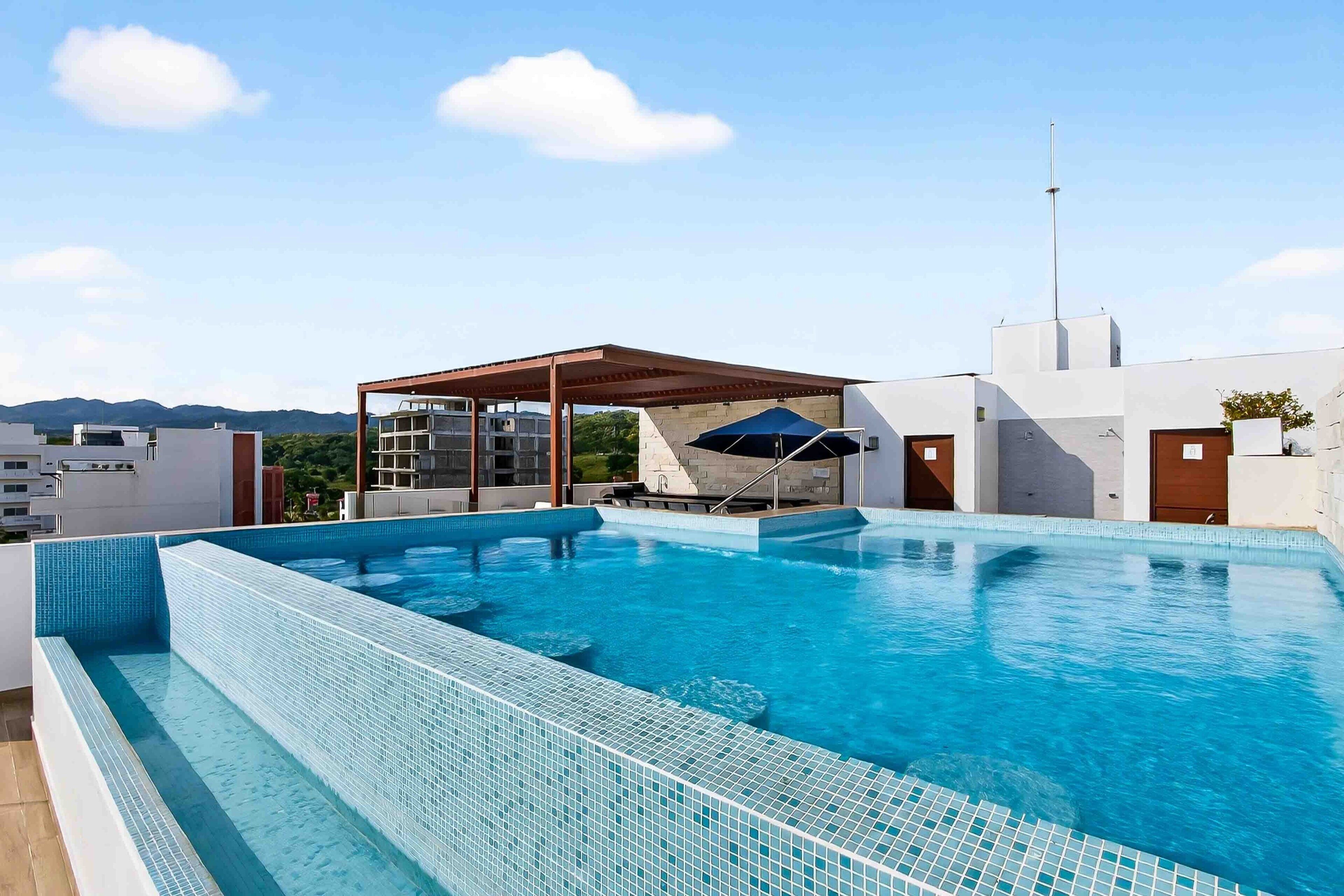 A rooftop swimming pool with clear blue water, a covered seating area, and a view of distant mountains.