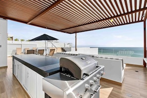 A rooftop bar with a grill, seating area, and a view of the ocean. - Relaxing Condo With Rooftop Pool, Oceanview Balcony & Walkable Beach Access (Bucerías)