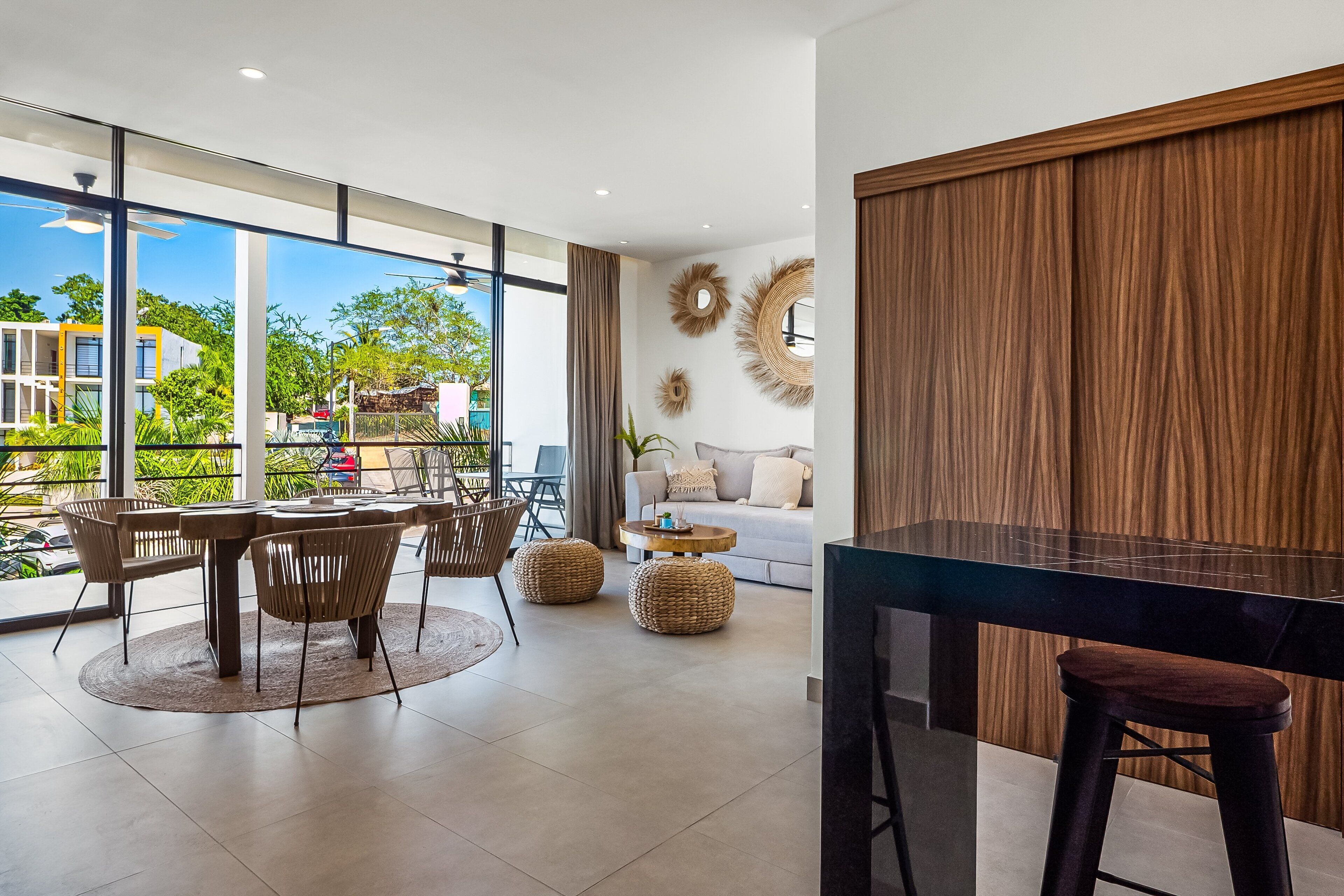 A modern interior with a dining area, a sofa, and a large window offering a view of greenery and buildings.