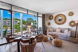 Ein modernes Wohnzimmer mit einem großen Fenster, einem grauen Sofa, Korbmöbeln und dekorativen Wandspiegeln.