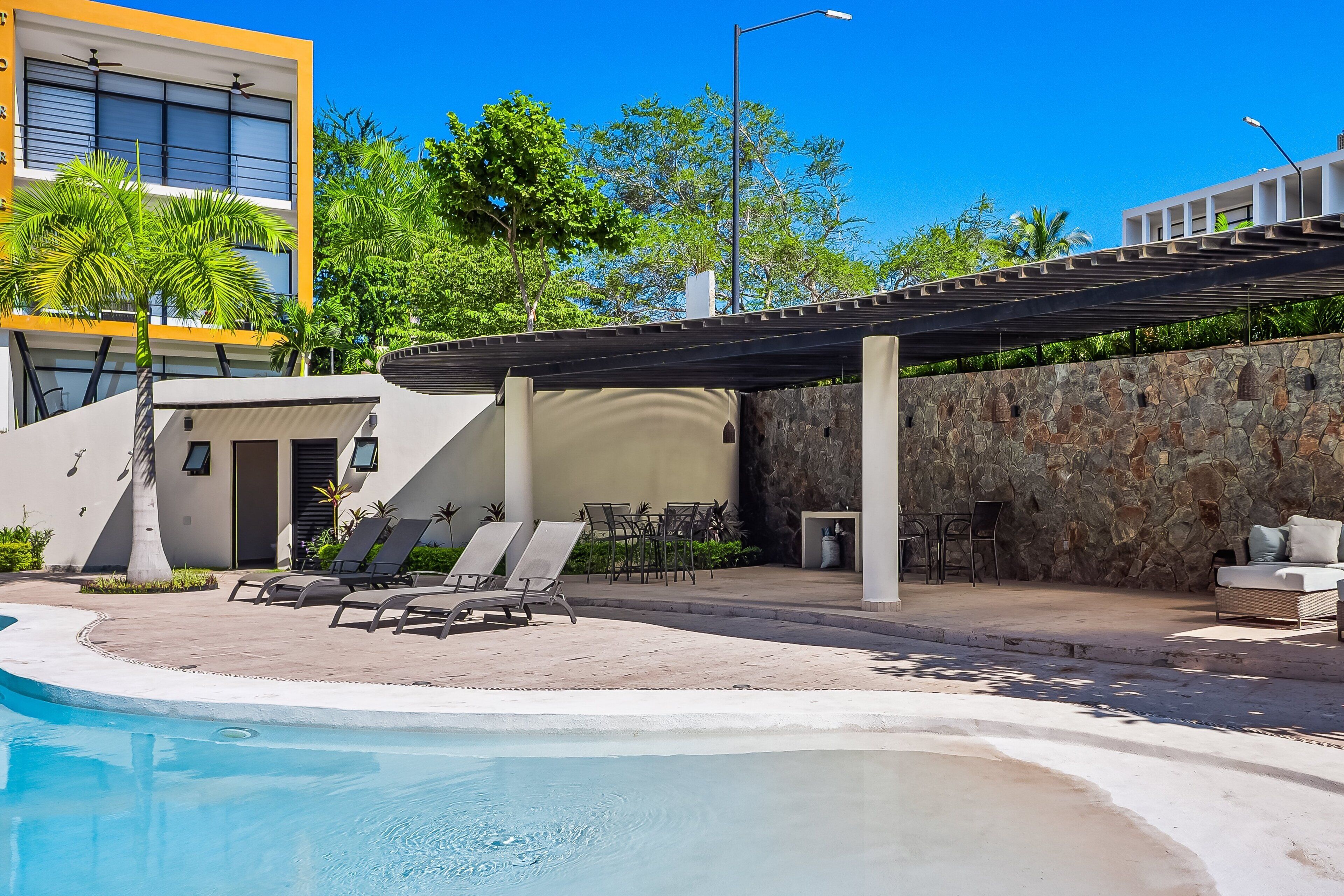A pool area with lounge chairs, a covered seating area, and a stone wall.