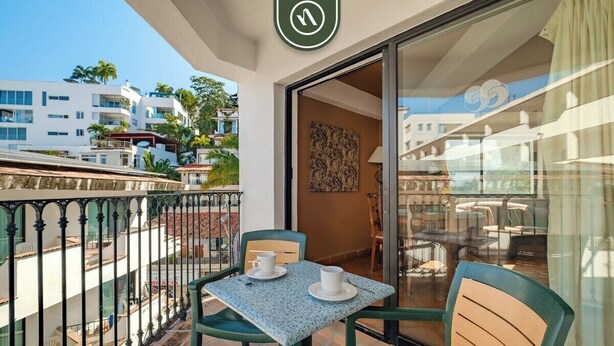 A balcony with a table and chairs, a sliding glass door, and a view of buildings and palm trees. - One Beach Street 307 B· Amazing 2 BR Condo (Puerto Vallarta)