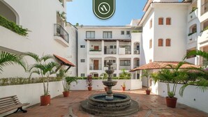 A courtyard with a central fountain, potted plants, and a bench. - One Beach Street 307 B· Amazing 2 BR Condo (Puerto Vallarta)