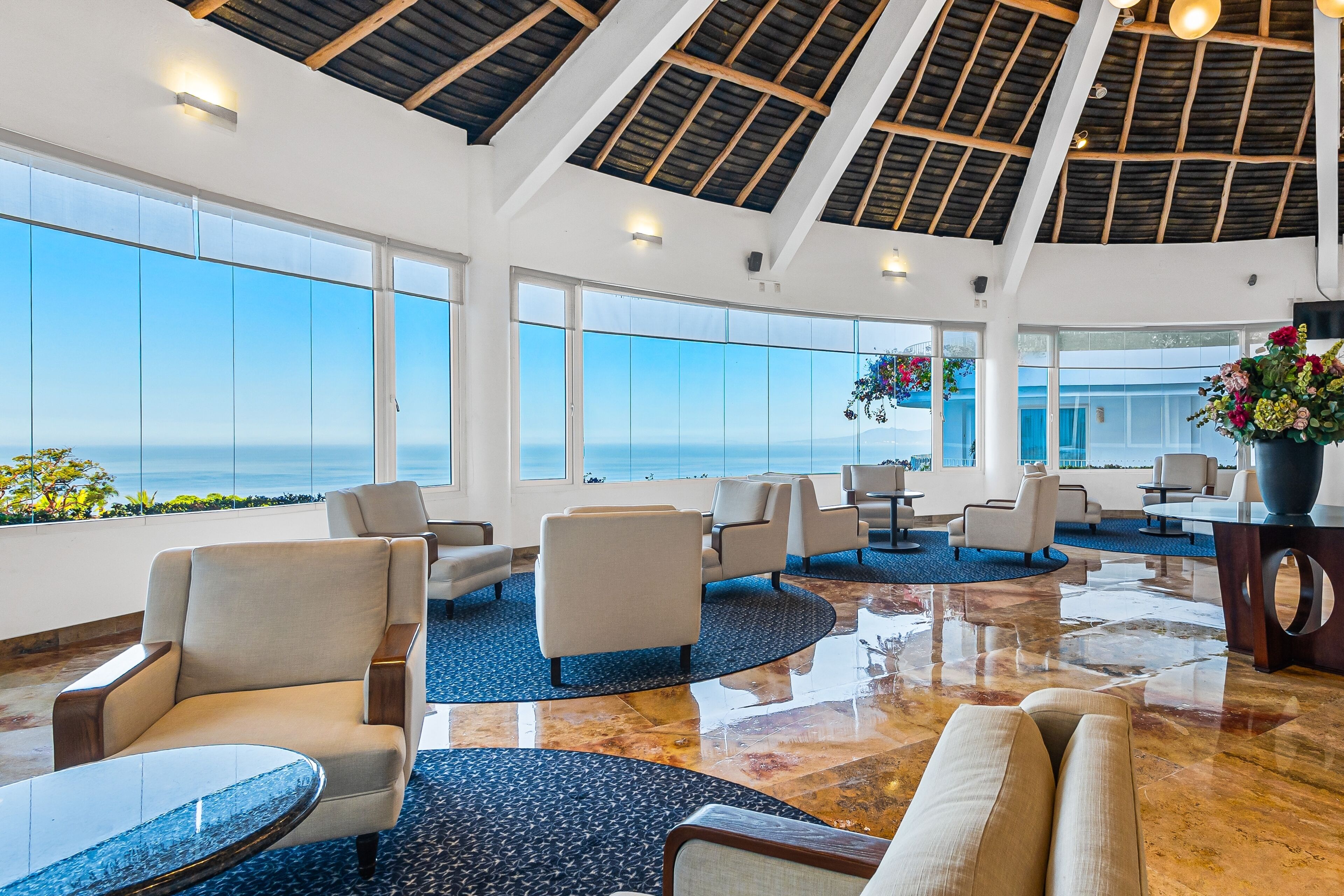 A spacious lobby with large windows offering ocean views, comfortable seating, and a polished floor.