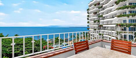 A balcony with a table and chairs, overlooking a body of water and a white building with balconies.