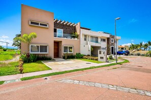 A modern multi-story residential building with a flat roof, large windows, and a well-maintained lawn. - Ocean-view Getaway With Patio, Grill, Roof Deck, & On-site Pools (La Cruz de Huanacaxtle)