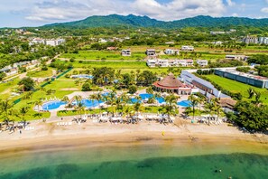 An aerial view of a resort with multiple swimming pools, a beach, and lush greenery.