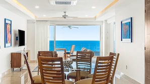 A dining area with a glass table and wooden chairs, a ceiling fan, and a view of the ocean. - Dreamy Coastal Condo With Amazing Ocean Views, Pool & Pool spa (Puerto Vallarta)