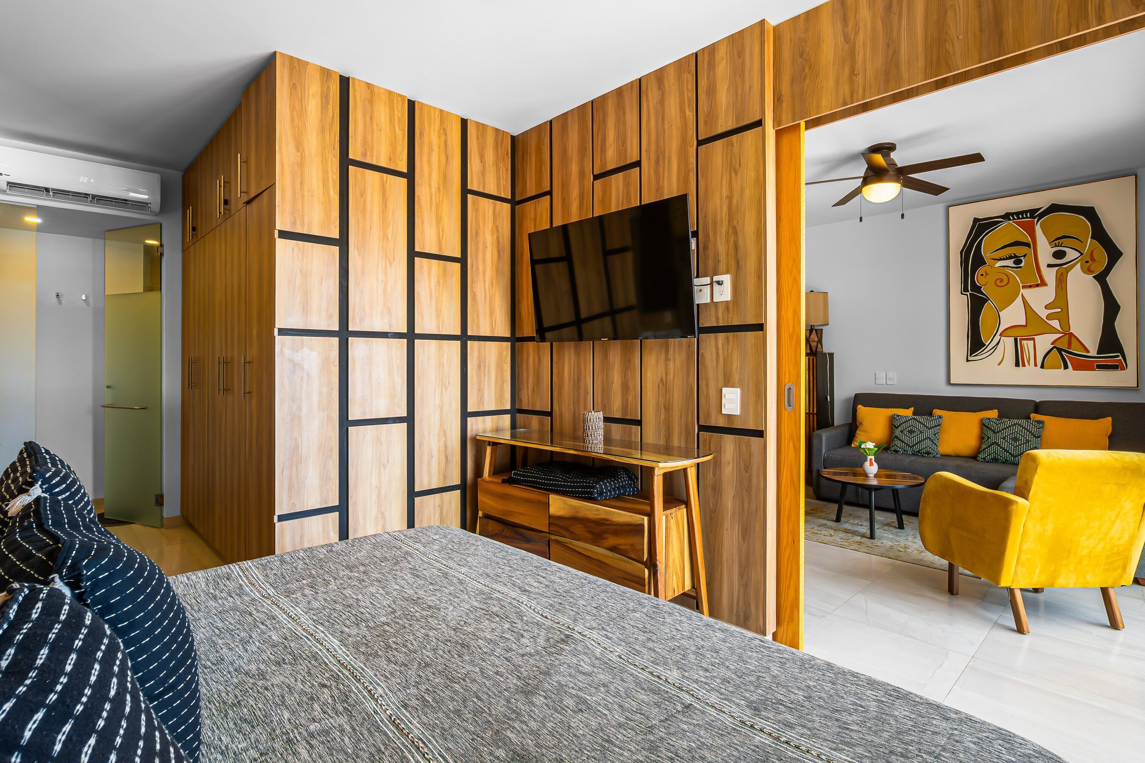 Une chambre moderne équipée d’un lit, d’un bureau, d’une télévision, d’un canapé et d’un fauteuil jaune.