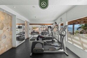 A modern gym with cardio equipment, a stone wall, and a view of the outdoors. - Peaceful Oceanview Studio - Costa Sur Estudio - 5 (Puerto Vallarta)