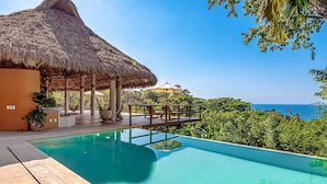 Una piscina con una estructura de techo de paja y vistas al océano.