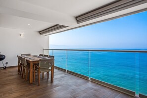 A balcony with a view of the sea, a dining table with chairs, and a grill. - Luxury Apartment With Infinity Pool, Ocean Views, Balcony & Easy Downtown Access (Puerto Vallarta)