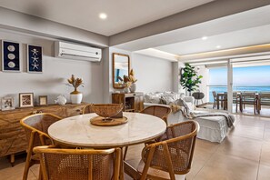 A modern living room with a round marble table, wicker chairs, a large mirror, and a view of the sea. - Luxury Apartment With Infinity Pool, Ocean Views, Balcony & Easy Downtown Access (Puerto Vallarta)