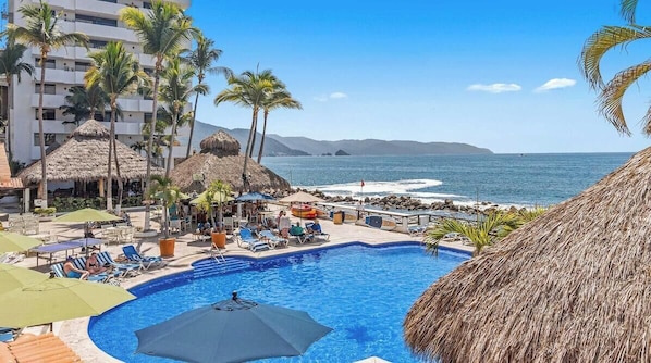 A pool area with lounge chairs, umbrellas, and a view of the ocean. - Peaceful Oceanview- Costa Sur Estudio 3 (Puerto Vallarta)