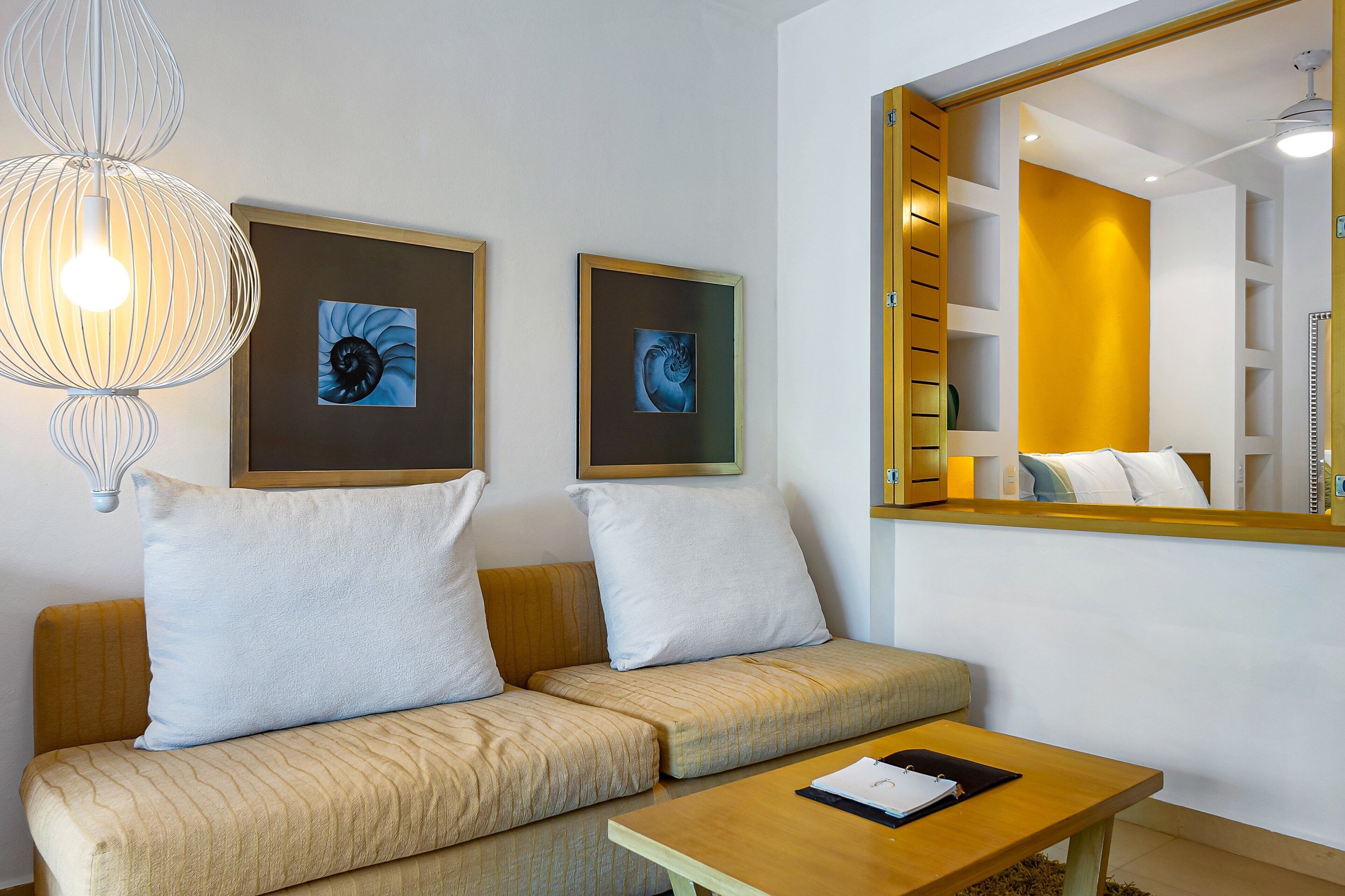 Una moderna camera d'albergo con un divano, un tavolino in legno e due opere d'arte incorniciate al muro.