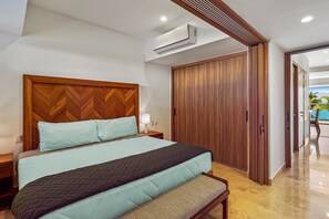 A modern hotel room with a large bed, a wooden headboard, a bench at the foot of the bed, a wardrobe, and an air conditioning unit. - Serene Coastal Getaway With Private Infinity Pool, Beach Access & Scenic Vistas (Puerto Vallarta)