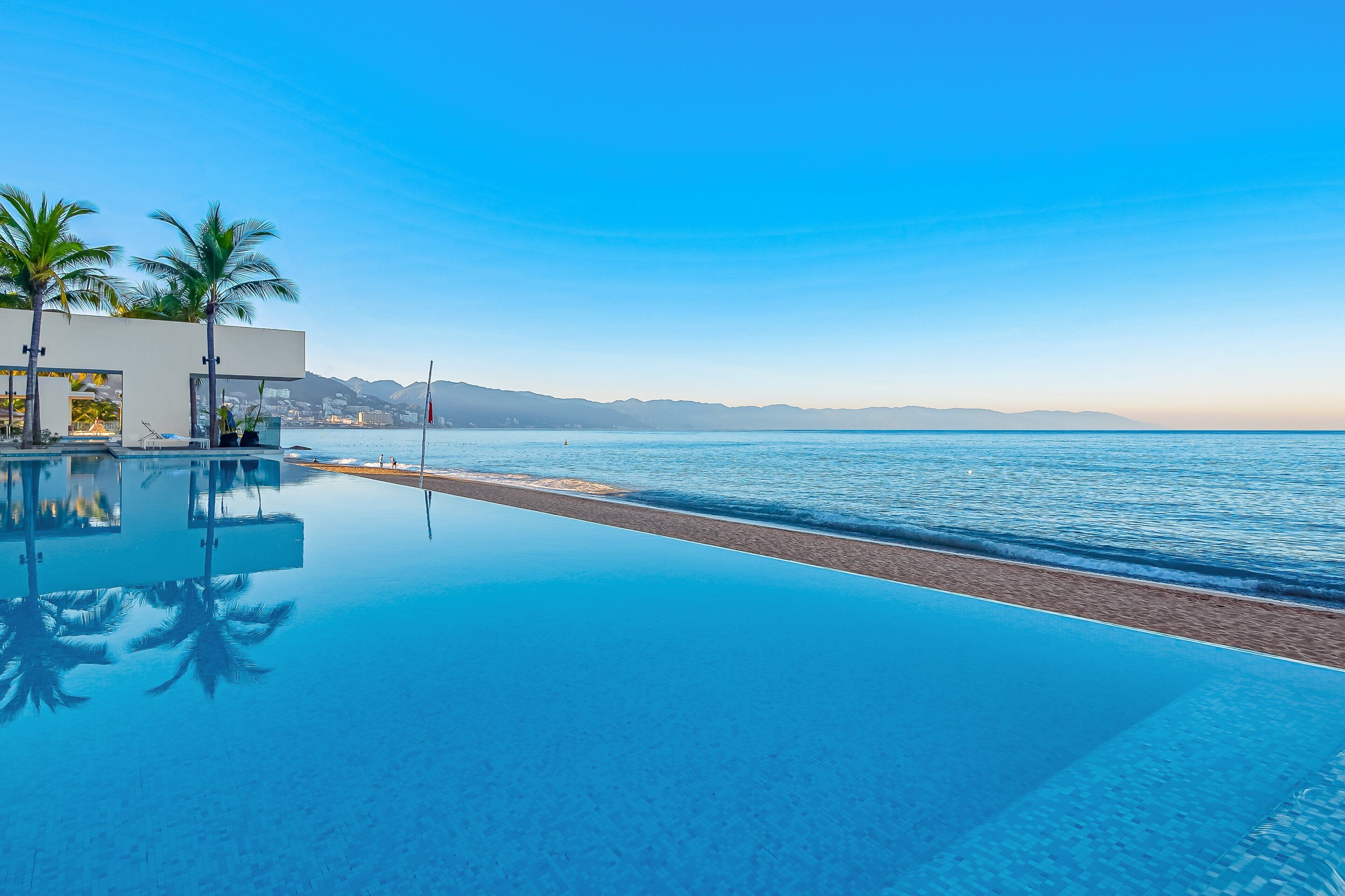 Une piscine à débordement moderne offrant une vue dégagée sur la plage et les montagnes en arrière-plan.
