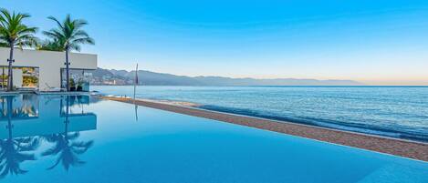 Une piscine à débordement moderne offrant une vue dégagée sur la plage et les montagnes en arrière-plan.