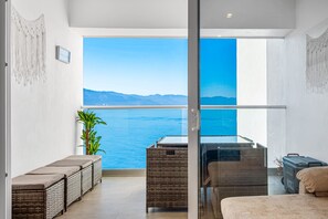 Ein Balkon mit Blick auf das Meer, Korbmöbel, ein Glastisch und ein Blumentopf.