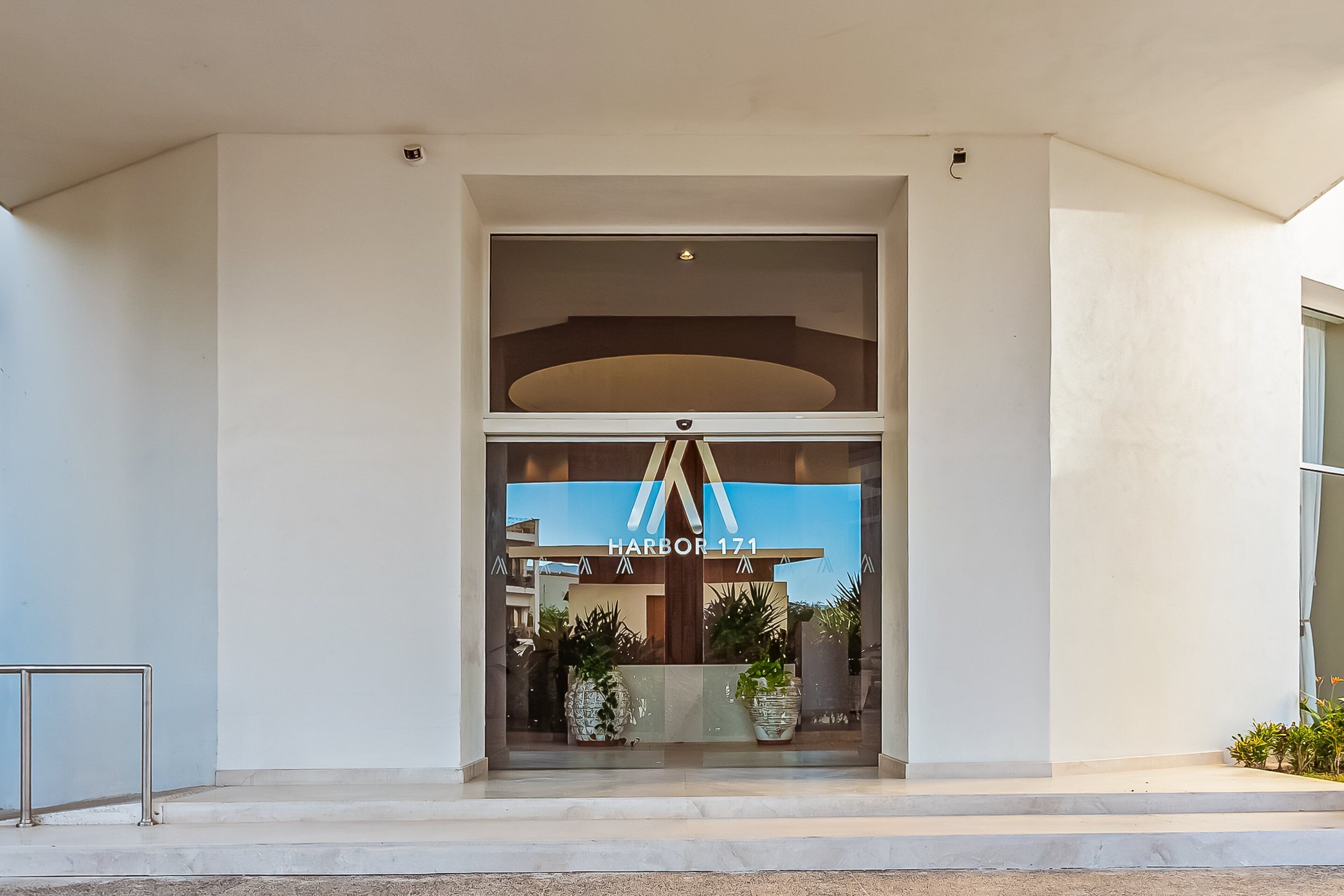A modern building entrance with a glass door, a sign reading 'HARBOR 171', and potted plants.