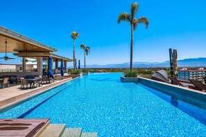 A swimming pool with lounge chairs and umbrellas, palm trees, and a view of distant mountains. - Peaceful Modern Condo With Rooftop Pool, Washer-dryer and Fitness Room (Nuevo Nayarit)