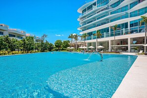 Un hotel moderno con una grande piscina, area salotto esterna e un edificio a più piani con balconi.