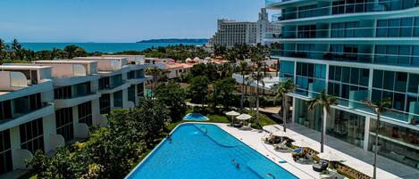 A resort with a large swimming pool, modern buildings, and a view of the ocean.