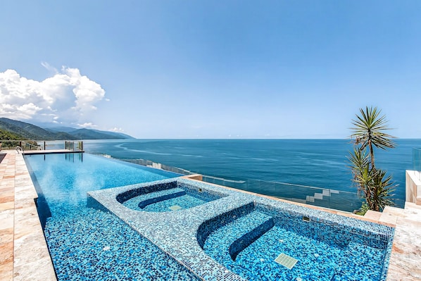 A infinity pool with a clear view of the ocean and mountains. - Modern Condo With Ocean Views, Rooftop Infinity Pool & Central AC (Puerto Vallarta)