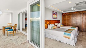 A hotel room with a bed, a desk with chairs, and a sliding glass door leading to a balcony. - Modern Condo With Ocean Views, Rooftop Infinity Pool & Central AC (Puerto Vallarta)