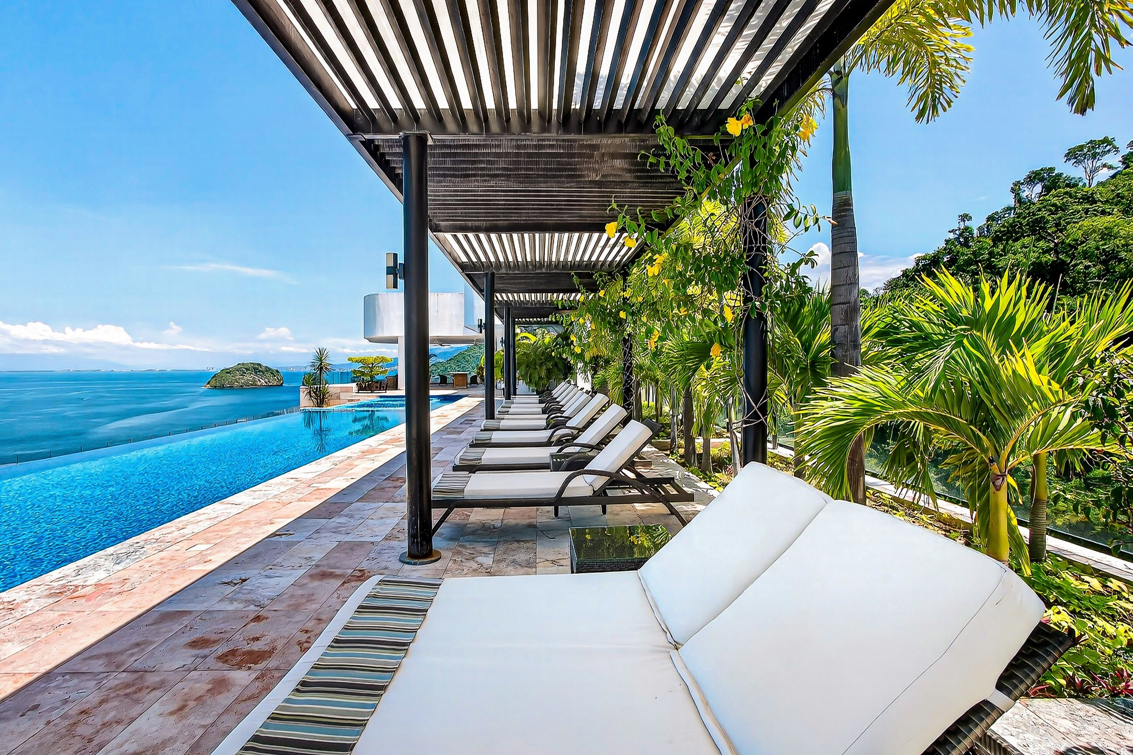 Un espace aménagé au bord de la piscine, avec des chaises longues, une pergola et une vue sur l’océan.