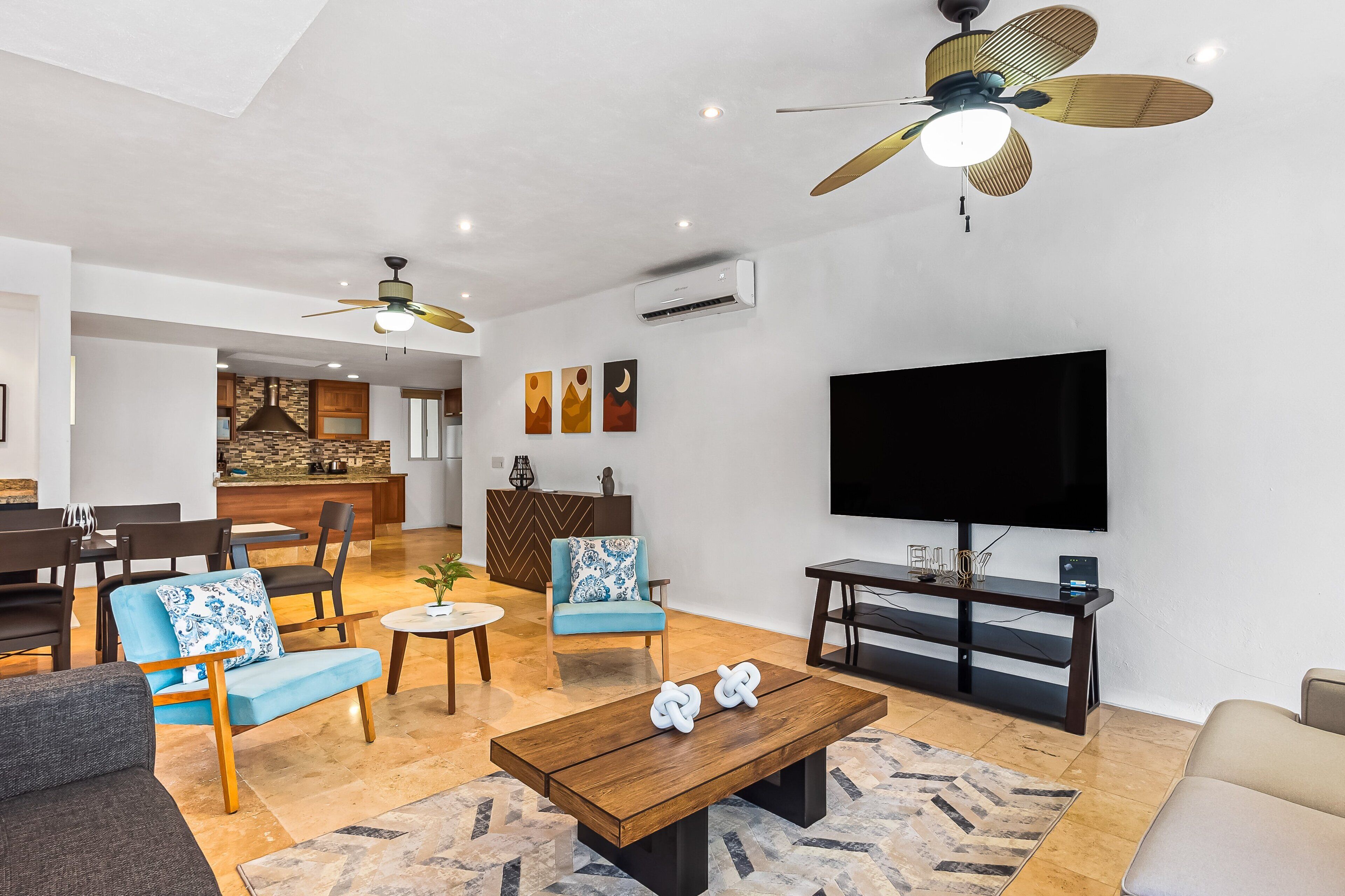 A modern living room with a flat-screen TV, ceiling fans, and a dining area with chairs and a table.