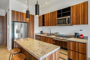 A modern kitchen with wooden cabinets, stainless steel appliances, granite countertops, and a central island with stools. - D'toscana Residencial, PH #11 Condo in Nuevo Vallarta With Rooftop Pool (Nuevo Nayarit)